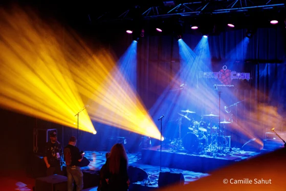 Scène de concert Basket Case avec éclairage spectaculaire en jaune et bleu, batterie au centre, techniciens autour. Photo par Camille Sahut.